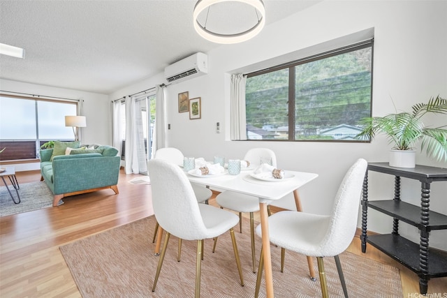 dining space with a wall mounted air conditioner, a textured ceiling, and wood finished floors