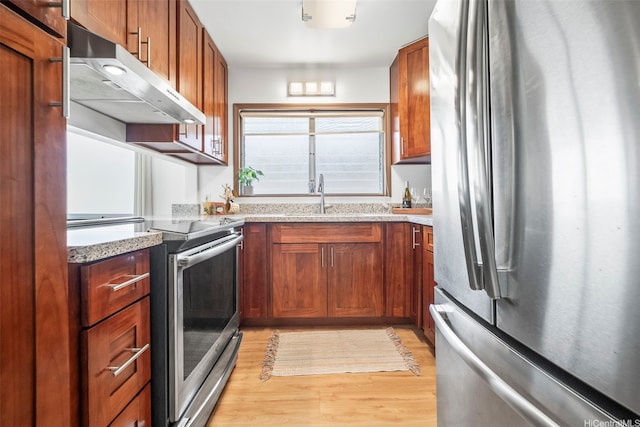 kitchen with light stone counters, a sink, light wood-type flooring, appliances with stainless steel finishes, and under cabinet range hood