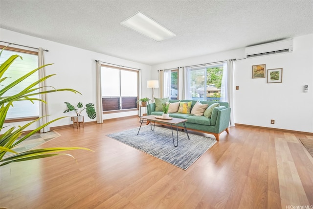 living area featuring baseboards, light wood-style floors, a textured ceiling, and a wall unit AC
