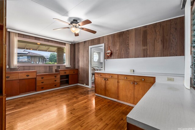 kitchen with ceiling fan, brown cabinetry, light wood-type flooring, wood walls, and light countertops