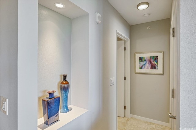 corridor featuring baseboards and light tile patterned flooring