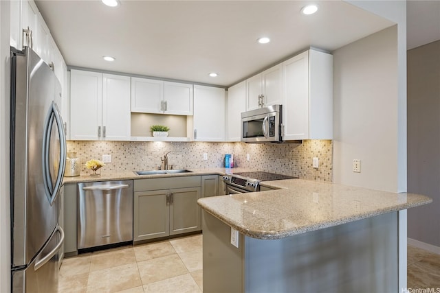 kitchen with backsplash, a sink, light stone counters, a peninsula, and stainless steel appliances