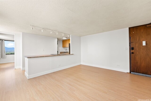 unfurnished living room featuring track lighting, light wood-type flooring, a textured ceiling, and baseboards