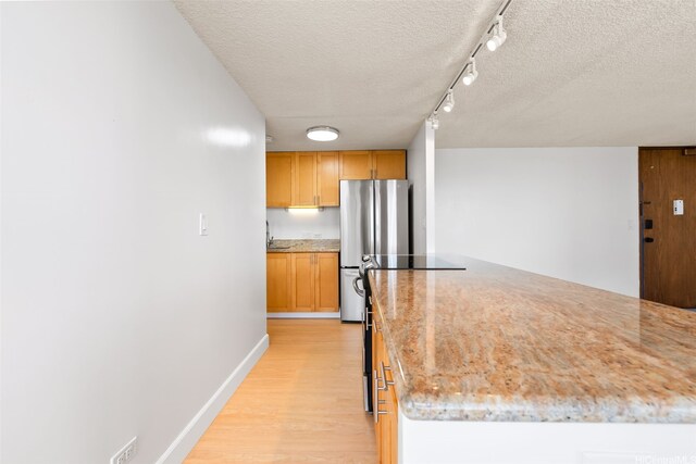 kitchen featuring a textured ceiling, light wood-type flooring, baseboards, light stone countertops, and freestanding refrigerator