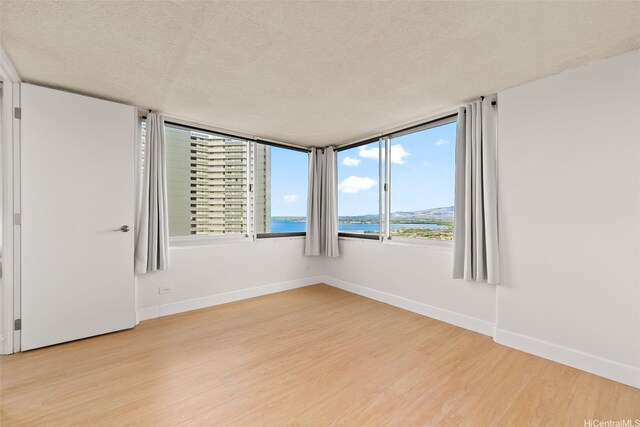 spare room with a textured ceiling, light wood-type flooring, a water view, and baseboards