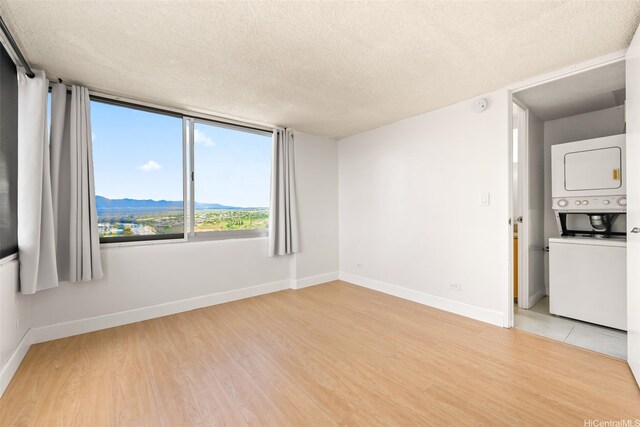 spare room with baseboards, stacked washer and dryer, a textured ceiling, and light wood-style flooring