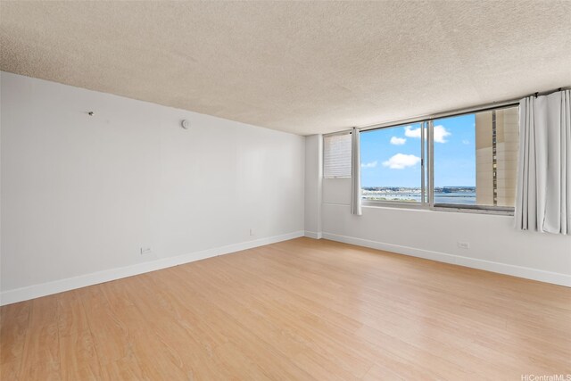 unfurnished room with baseboards, light wood-style floors, and a textured ceiling