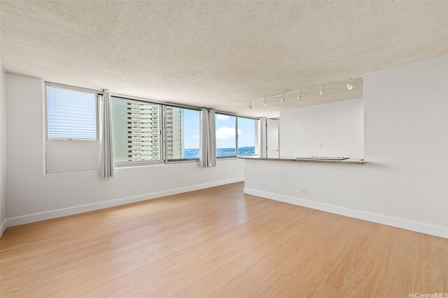 spare room with baseboards, a textured ceiling, and light wood-style flooring