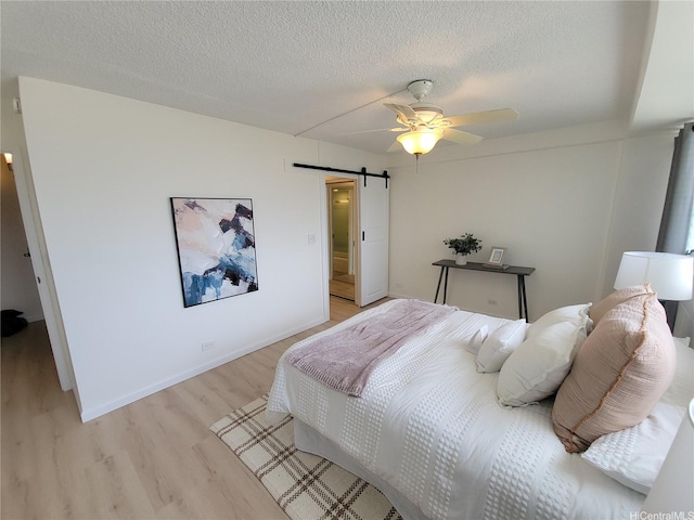 1615 Wilder Ave Unit 604, Honolulu, HI 96822 - bedroom featuring a barn door, light wood finished floors, a textured ceiling, a ceiling fan, and baseboards