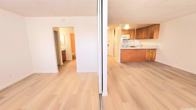 kitchen with baseboards, white microwave, light countertops, brown cabinets, and light wood finished floors