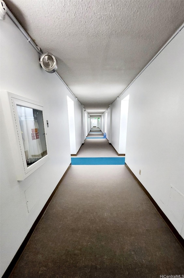 corridor featuring carpet floors, a textured ceiling, and baseboards