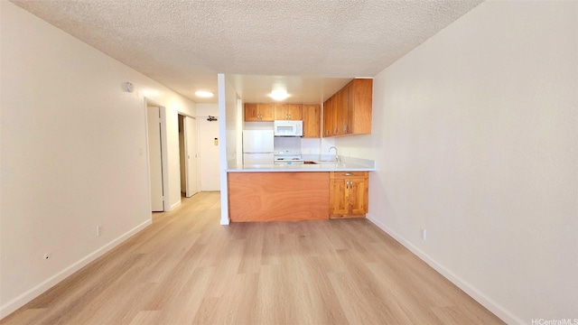 kitchen featuring baseboards, light wood finished floors, brown cabinets, and white appliances