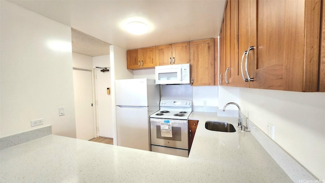 kitchen with a sink, brown cabinetry, white appliances, and light stone countertops
