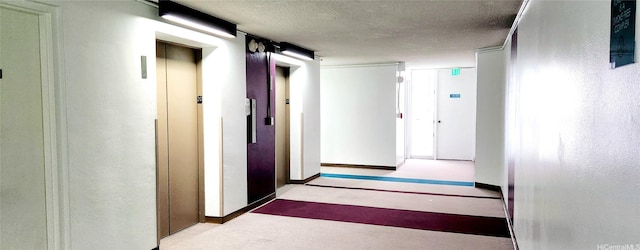 hallway with a textured ceiling, baseboards, and elevator