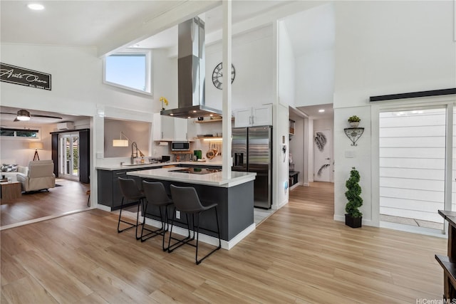 kitchen featuring high vaulted ceiling, a kitchen breakfast bar, island exhaust hood, stainless steel appliances, and light countertops