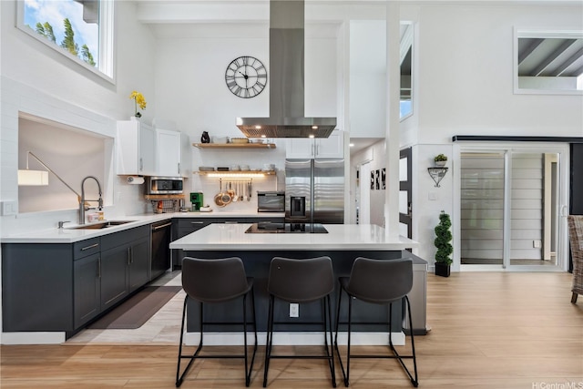 kitchen with stainless steel appliances, a kitchen breakfast bar, island exhaust hood, a sink, and a towering ceiling