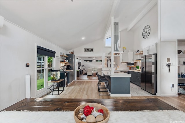 kitchen with light wood-type flooring, appliances with stainless steel finishes, light countertops, high vaulted ceiling, and a breakfast bar area