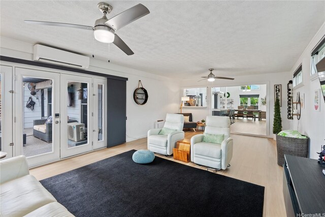 living area with an AC wall unit, a ceiling fan, wood finished floors, a textured ceiling, and french doors