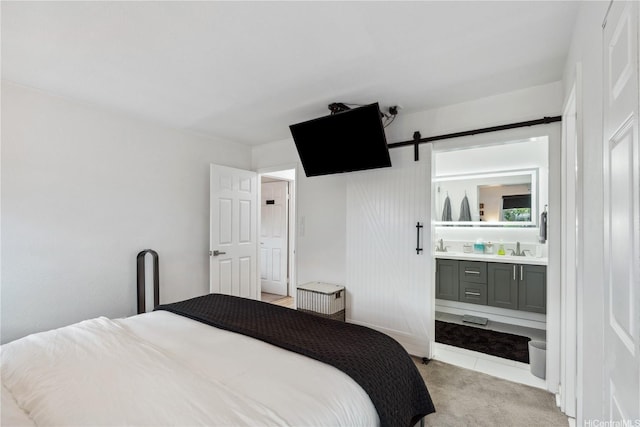 bedroom featuring light colored carpet, a barn door, ensuite bathroom, and a sink