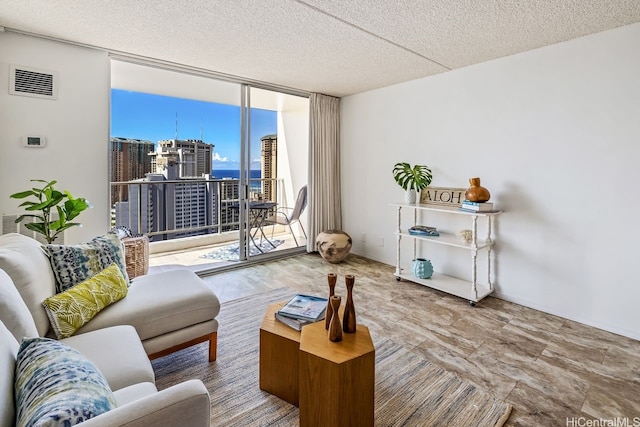 living room with a textured ceiling, visible vents, a wall of windows, and a city view