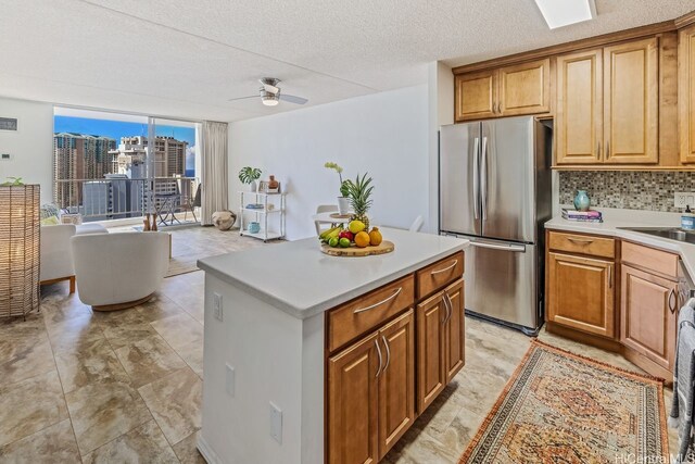 kitchen with decorative backsplash, a center island, a ceiling fan, light countertops, and freestanding refrigerator