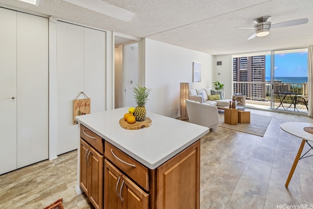 kitchen featuring brown cabinetry, light countertops, a kitchen island, ceiling fan, and a textured ceiling