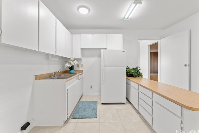 kitchen with freestanding refrigerator, light countertops, white cabinets, a sink, and a peninsula