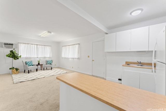 kitchen featuring carpet flooring, a wall mounted air conditioner, light countertops, white cabinets, and freestanding refrigerator