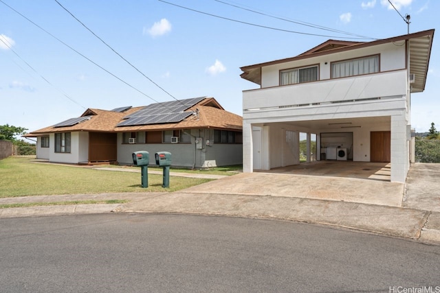 view of front facade with driveway, roof mounted solar panels, a carport, washer / dryer, and a front lawn