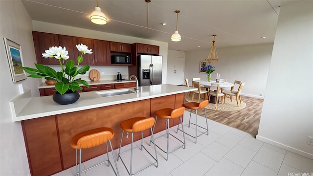 kitchen with light countertops, stainless steel refrigerator with ice dispenser, black microwave, and a sink