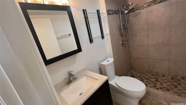 bathroom with toilet, a tile shower, and vanity