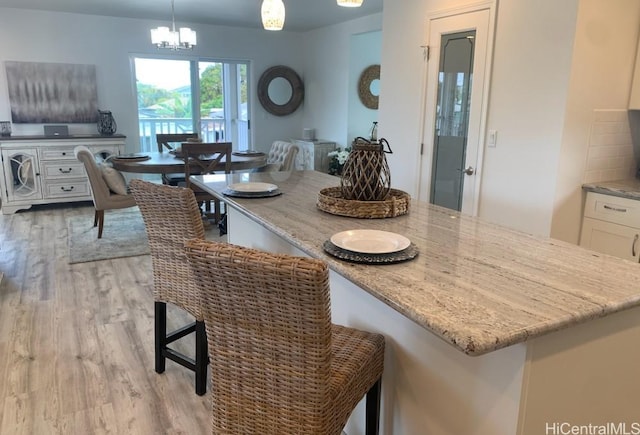 kitchen with hanging light fixtures, a breakfast bar area, light wood-type flooring, white cabinetry, and light stone countertops