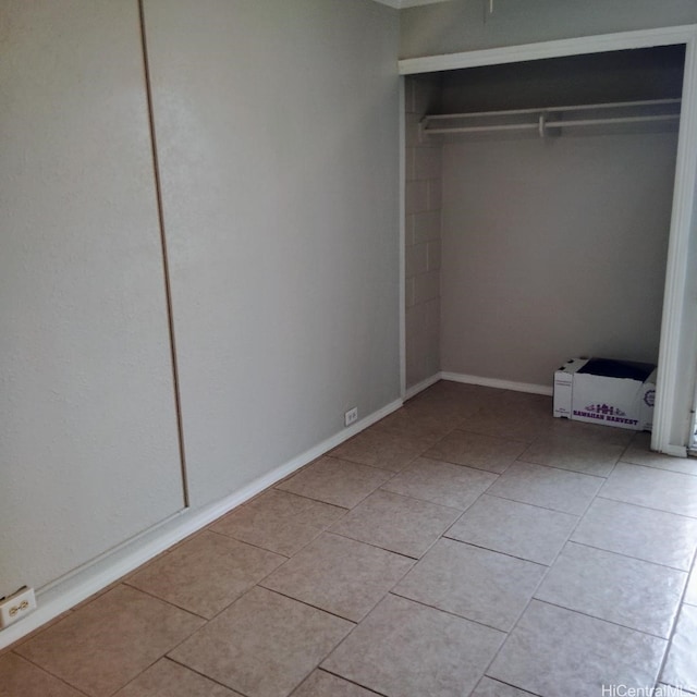 unfurnished bedroom featuring light tile patterned floors, baseboards, and a closet