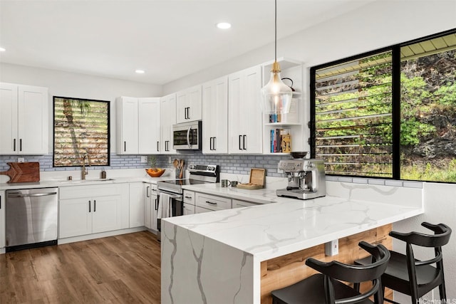 kitchen with light stone counters, decorative backsplash, a sink, appliances with stainless steel finishes, and a peninsula