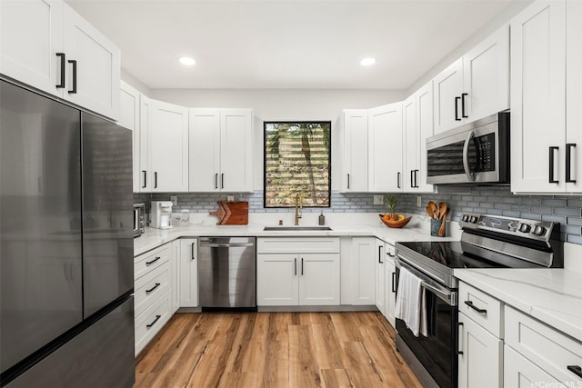 kitchen featuring a sink, stainless steel appliances, light wood-style floors, tasteful backsplash, and white cabinetry