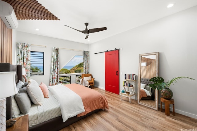 bedroom with a barn door, a wall unit AC, light wood finished floors, and recessed lighting