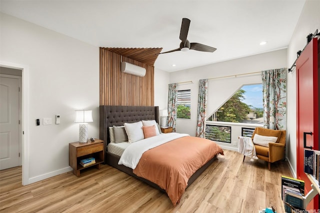 bedroom featuring a barn door, a wall unit AC, light wood-type flooring, and recessed lighting