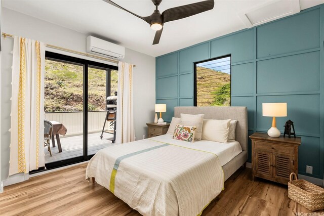 bedroom featuring light wood-style floors, attic access, a wall mounted AC, a decorative wall, and access to outside