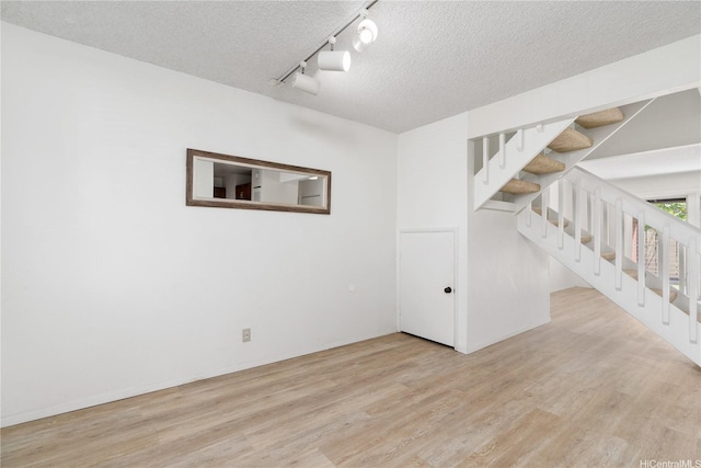 unfurnished room with wood finished floors, rail lighting, baseboards, a textured ceiling, and stairs