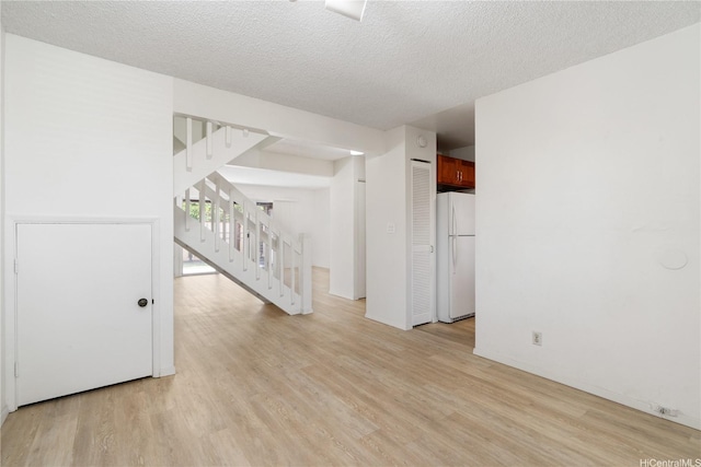 spare room featuring light wood-type flooring, a textured ceiling, and stairs