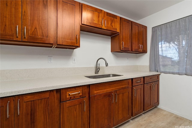 kitchen with brown cabinets, light wood-type flooring, light stone countertops, and a sink