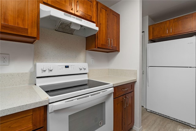 kitchen featuring light wood finished floors, under cabinet range hood, white appliances, and brown cabinetry