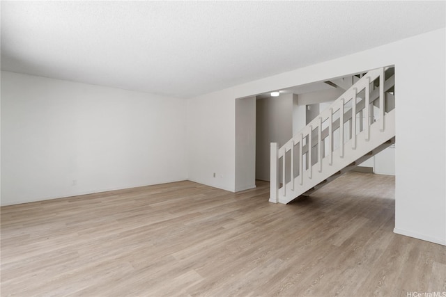 spare room with stairway and light wood-style floors
