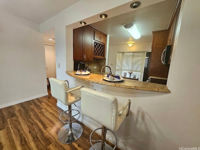 kitchen with a kitchen breakfast bar, stainless steel microwave, decorative backsplash, baseboards, and dark wood-style flooring