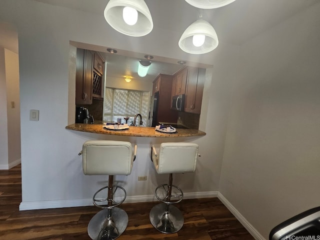 kitchen with a kitchen breakfast bar, stainless steel microwave, fridge, baseboards, and dark wood-type flooring