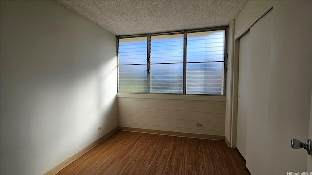 empty room featuring a textured ceiling, concrete block wall, dark wood-type flooring, and baseboards