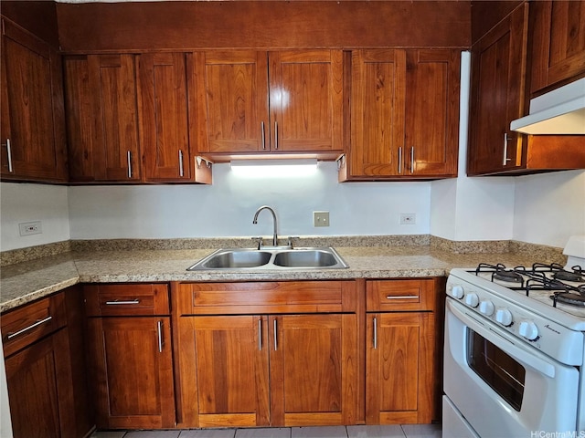 kitchen with light stone counters, white gas range oven, a sink, under cabinet range hood, and brown cabinetry