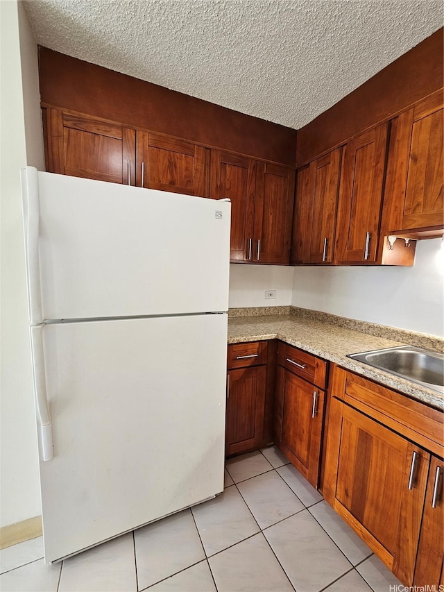 kitchen with freestanding refrigerator, light tile patterned floors, light countertops, a sink, and a textured ceiling