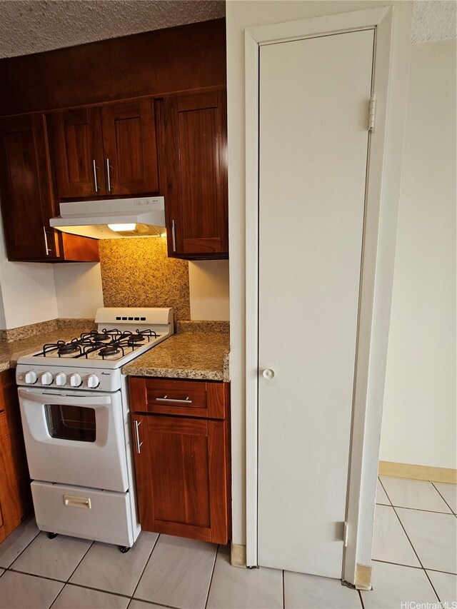 kitchen with light tile patterned flooring, under cabinet range hood, and gas range gas stove