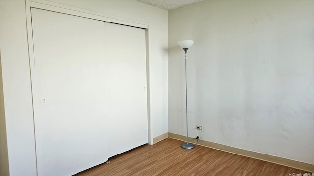 unfurnished bedroom featuring wood finished floors, baseboards, and a closet